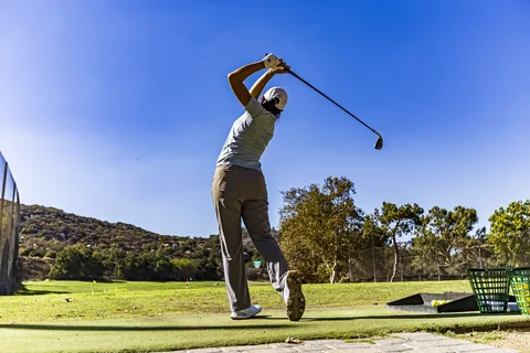 A golfer at the top of her backswing on the range tee, under a deep blue sky