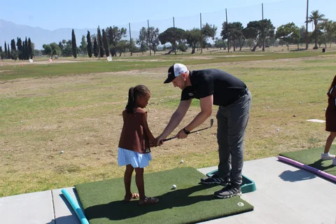 Coach Jon bends down to help a young girl with her grip on the range mat
