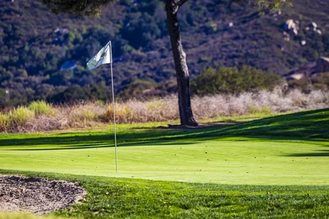 A green with its flag, a bunker and sunlit hills behind