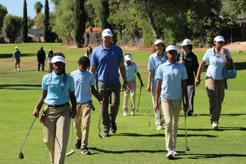 Coach Jon walks down the fairway with a group of junior golfers, clubs in hand