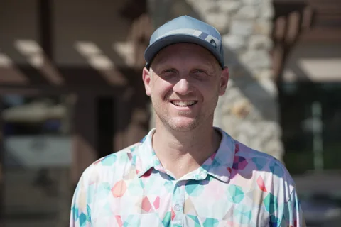 Coach Jon Flietstra, smiling, in a blue cap and a colorful patterned golf shirt