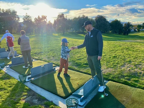 Coach Jon shakes hands with a young golfer on the range in the late-afternoon sun